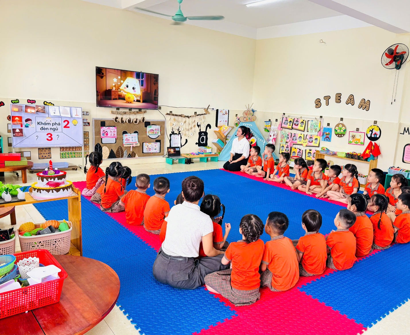 'A group of children sitting on the floor in a classroom
Description automatically generated'